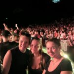Drei Frauen hinter einer Bartheke bei einem Konzert abends mit Publikum im Hintergrund
