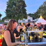 Zwei Frauen hinter einer Bartheke bei einem Konzert abends mit Publikum im Hintergrund