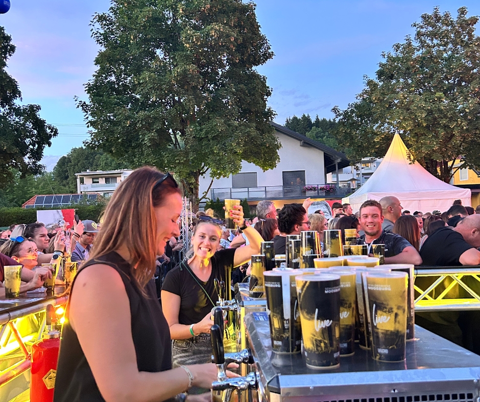 Zwei Frauen hinter einer Bartheke bei einem Konzert abends mit Publikum im Hintergrund