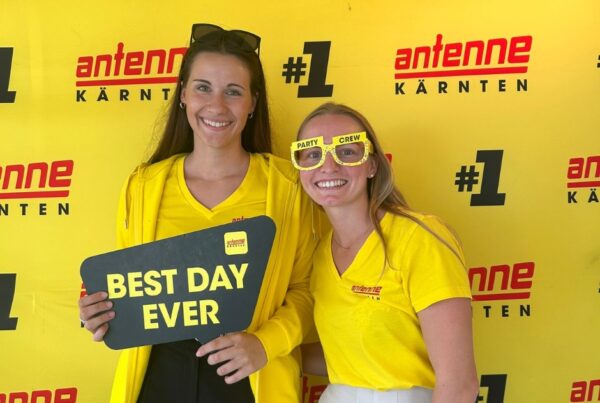 Zwei Frauen mit einem Schild "Best Day Ever" vor einer Antenne Kärnten Werbewand