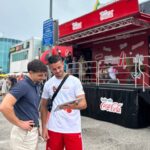 Zwei junge Männer, die auf ein iPad vor einer Coca Cola Bühne schauen.