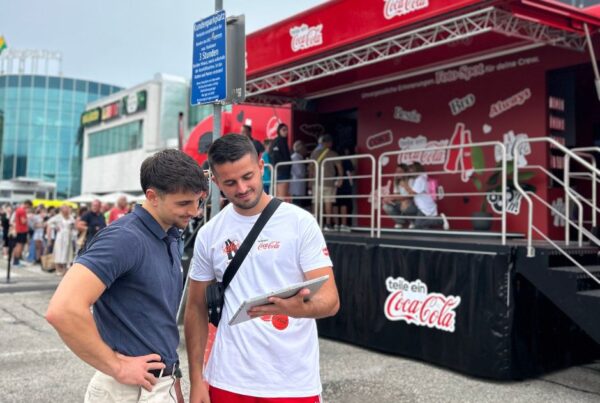 Zwei junge Männer, die auf ein iPad vor einer Coca Cola Bühne schauen.