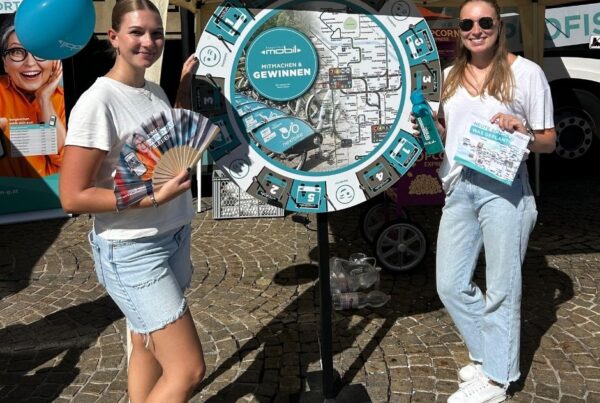 Zwei Promoterinnen stehen vor einem Glücksrad mit Flyern in der Hand