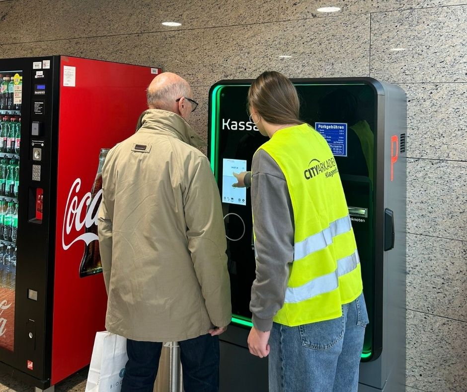 Frau erklärt am Parkautomaten neues Parkleitsystem einem Herrn